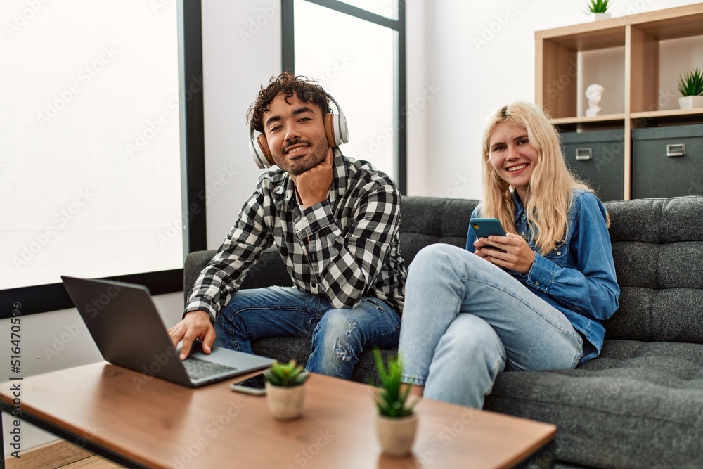 Fototapeta premium Young couple smling happy using laptop and smartphone at home.
