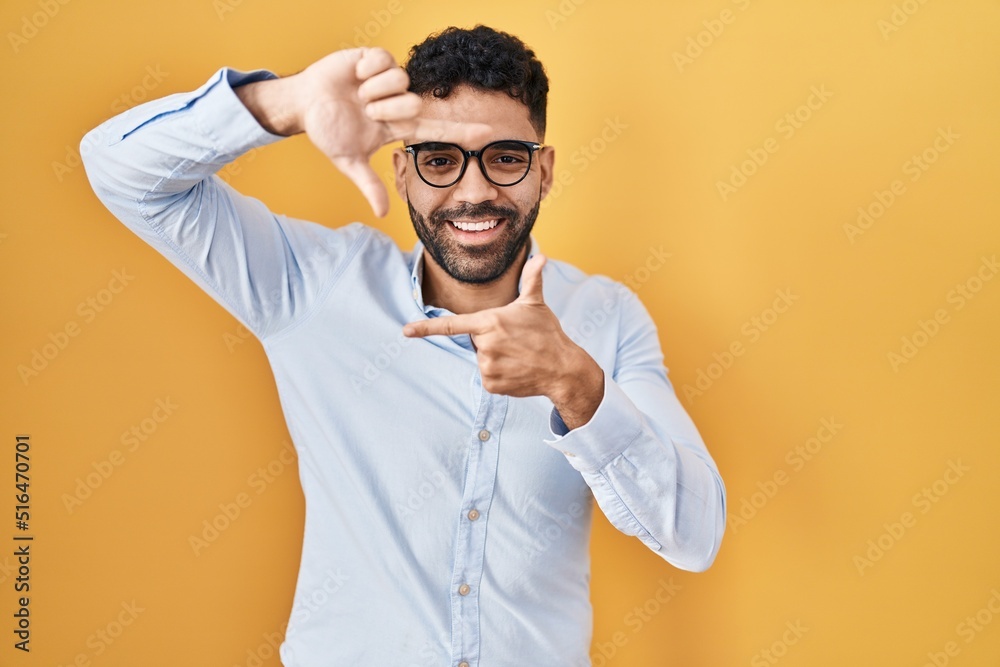 Hispanic man with beard standing over yellow background smiling making frame with hands and fingers with happy face. creativity and photography concept. Hispanic man with beard standing over yellow background smiling making frame with hands and fingers with happy face. creativity and photography concept.