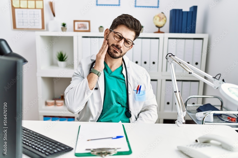 Young man with beard wearing doctor uniform and stethoscope at the clinic touching mouth with hand with painful expression because of toothache or dental illness on teeth. dentist Young man with beard wearing doctor uniform and stethoscope at the clinic touching mouth with hand with painful expression because of toothache or dental illness on teeth. dentist