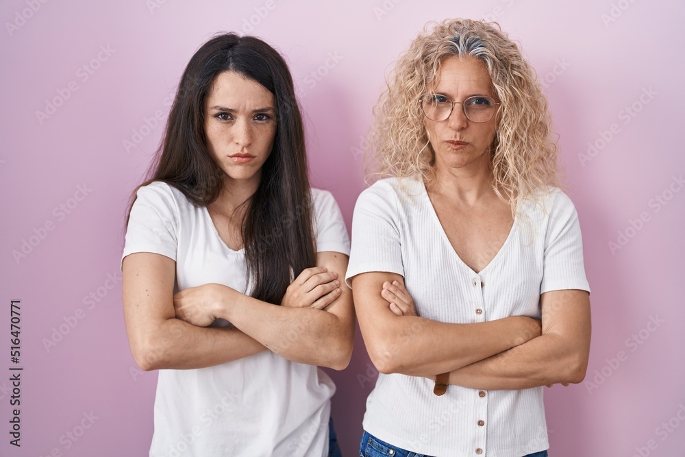 Mother and daughter standing together over pink background skeptic and nervous, disapproving expression on face with crossed arms. negative person. Mother and daughter standing together over pink background skeptic and nervous, disapproving expression on face with crossed arms. negative person.