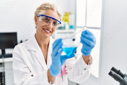 Middle age blonde woman wearing scientist uniform holding test tube at laboratory