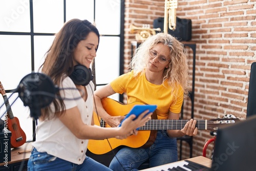 Two women musicians playing classical guitar looking touchpad at music studio