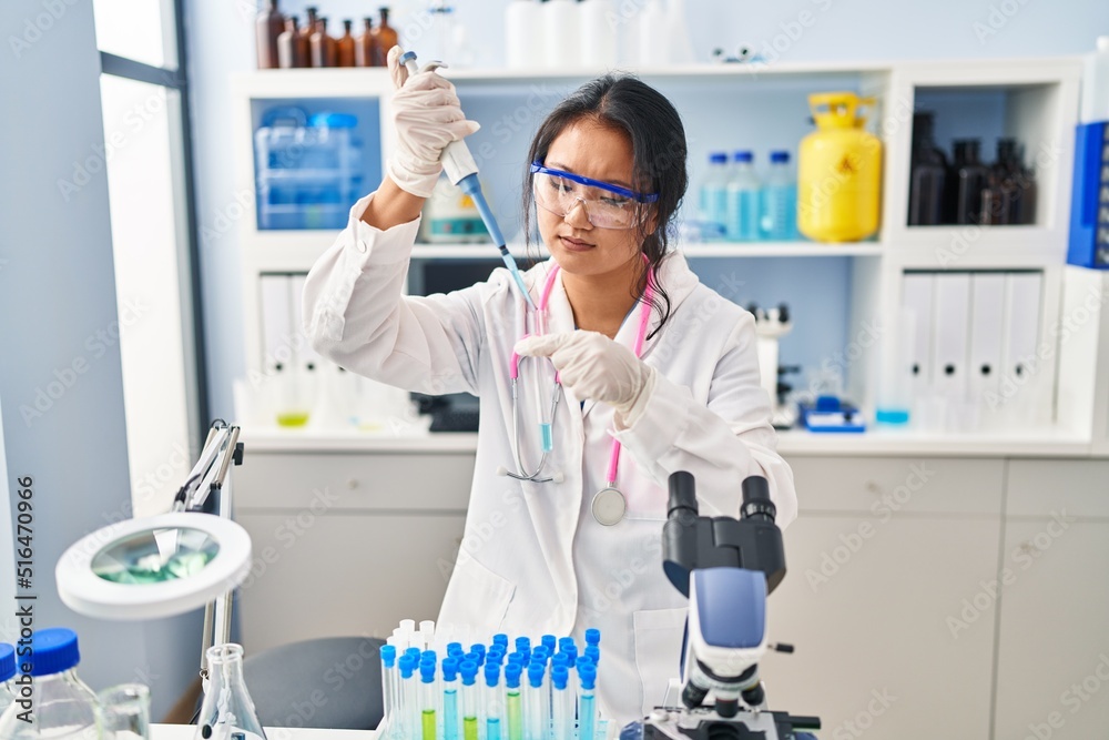 Fototapeta premium Young chinese woman wearing scientist uniform working at laboratory