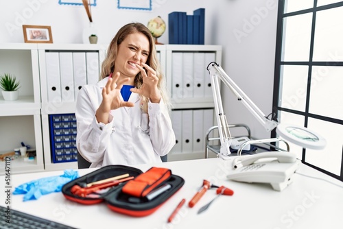Young beautiful doctor woman with reflex hammer and medical instruments disgusted expression, displeased and fearful doing disgust face because aversion reaction. with hands raised