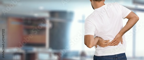 Man stand, touch lower back, suffer from sudden backache, due to uncomfortable chair. Sedentary work disease, rheumatism, low-back lumbar pain illness concept photo