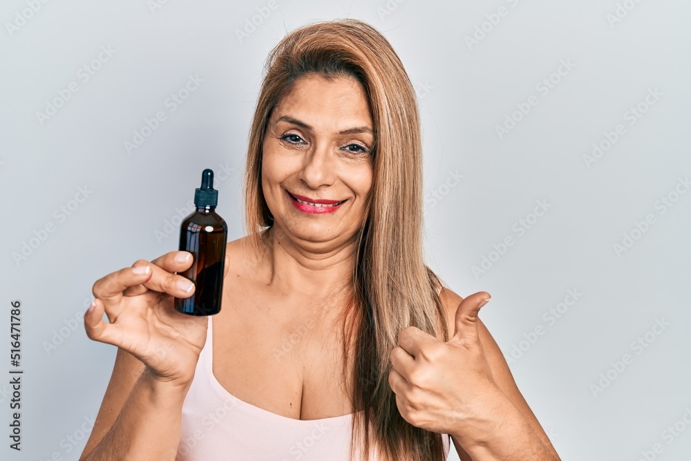 Middle age hispanic woman using night serum smiling happy and positive, thumb up doing excellent and approval sign Middle age hispanic woman using night serum smiling happy and positive, thumb up doing excellent and approval sign