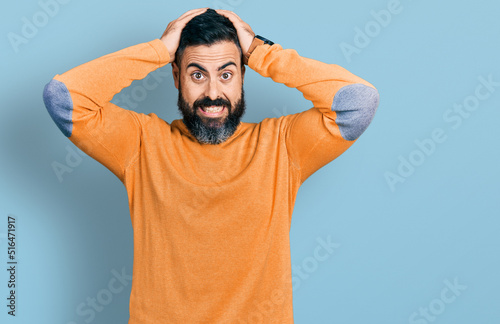 Hispanic man with beard wearing casual winter sweater crazy and scared with hands on head, afraid and surprised of shock with open mouth