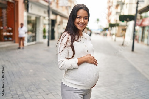 Young latin woman pregnant smiling confident touching belly at street photo