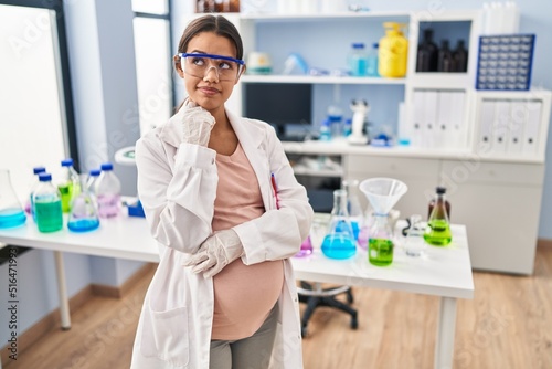 Young pregnant woman working at scientist laboratory serious face thinking about question with hand on chin  thoughtful about confusing idea