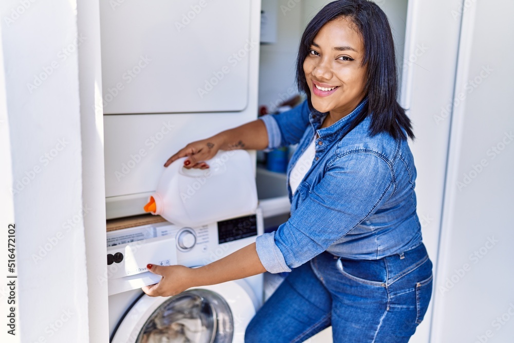 Hispanic brunette woman putting detergent into mashing machine at laundry room Hispanic brunette woman putting detergent into mashing machine at laundry room