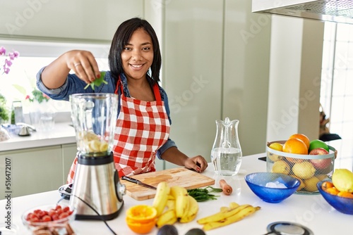 Hispanic brunette woman preparing fruit smoothie at the kitchen