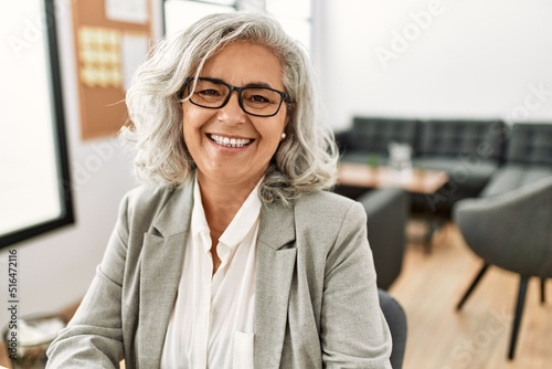 Middle age grey-haired businesswoman smiling happy working at the office. photo