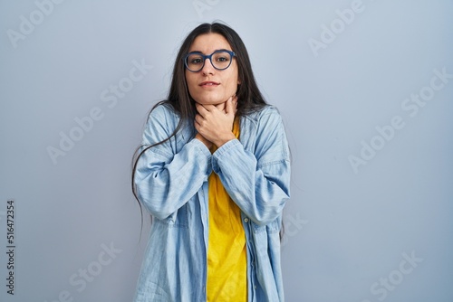 Young hispanic woman standing over blue background shouting suffocate because painful strangle. health problem. asphyxiate and suicide concept.