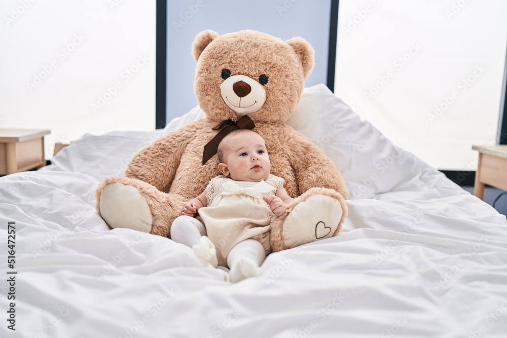 Adorable baby relaxed lying on bed with teddy bear at bedroom