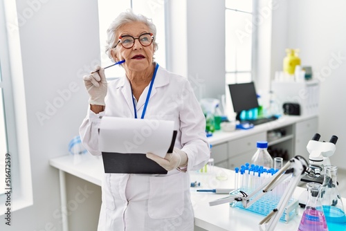 Senior grey-haired woman wearing scientist uniform with doubt expression at laboratory