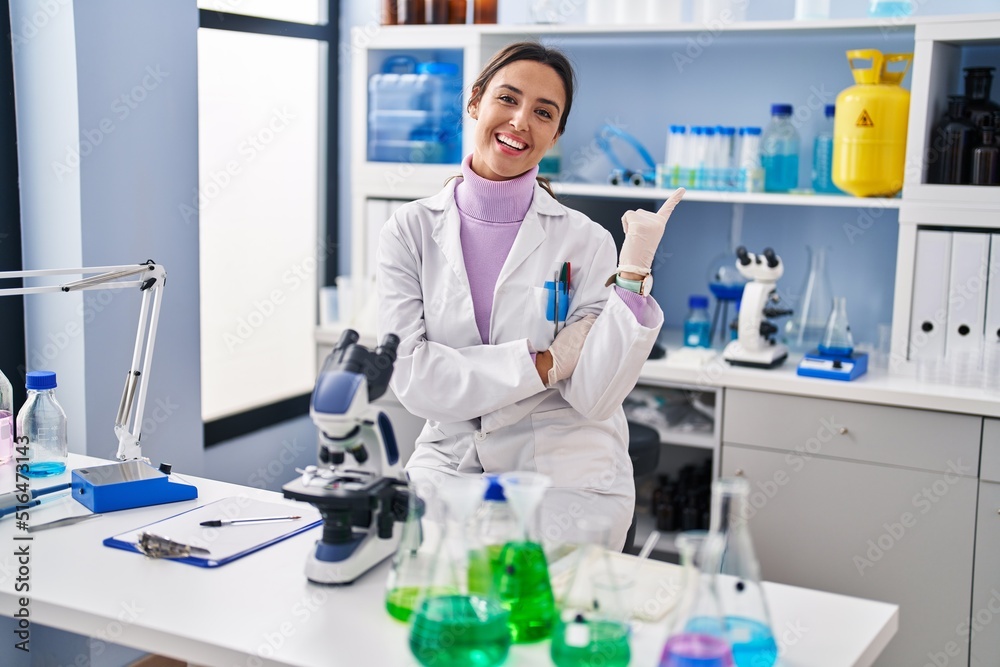 Young brunette woman working at scientist laboratory smiling happy pointing with hand and finger to the side Young brunette woman working at scientist laboratory smiling happy pointing with hand and finger to the side