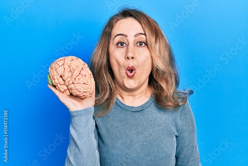 Middle age caucasian woman holding brain scared and amazed with open mouth for surprise, disbelief face