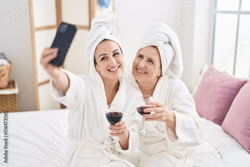 Mother and daughter make selfie by the smartphone drinking glass of wine at bedroom