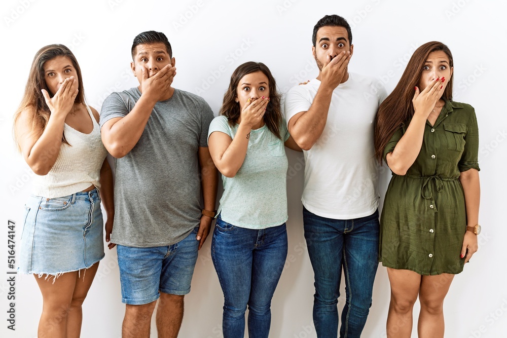 Group of young hispanic friends standing together over isolated background shocked covering mouth with hands for mistake. secret concept. Group of young hispanic friends standing together over isolated background shocked covering mouth with hands for mistake. secret concept.