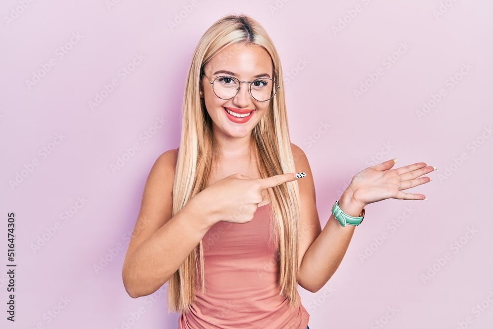 Young blonde girl wearing casual clothes amazed and smiling to the camera while presenting with hand and pointing with finger. Young blonde girl wearing casual clothes amazed and smiling to the camera while presenting with hand and pointing with finger.