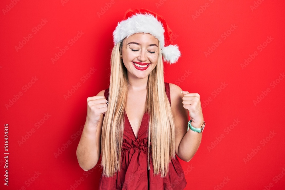Young blonde girl wearing christmas hat excited for success with arms raised and eyes closed celebrating victory smiling. winner concept. Young blonde girl wearing christmas hat excited for success with arms raised and eyes closed celebrating victory smiling. winner concept.