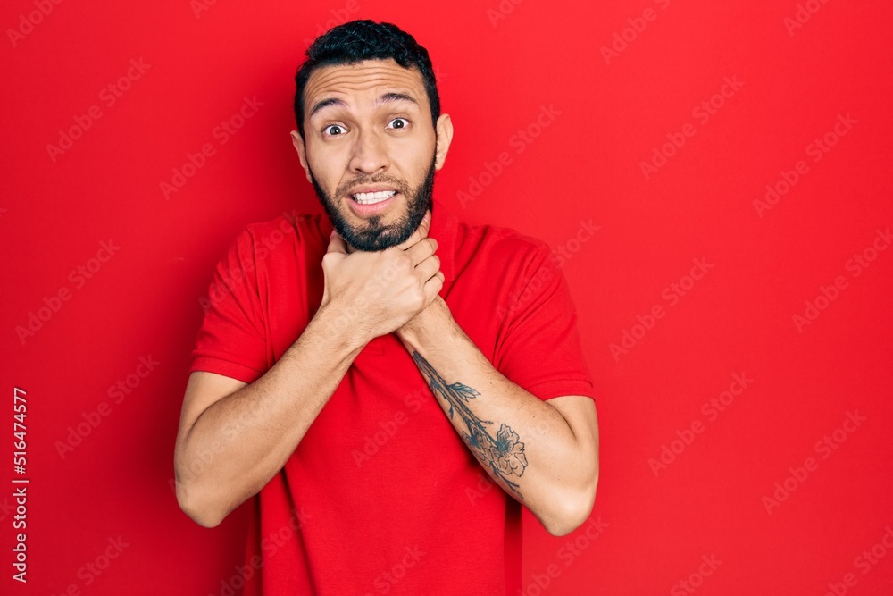 Hispanic man with beard wearing casual red t shirt shouting and suffocate because painful strangle. health problem. asphyxiate and suicide concept. Hispanic man with beard wearing casual red t shirt shouting and suffocate because painful strangle. health problem. asphyxiate and suicide concept.