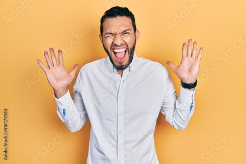 Hispanic man with beard wearing business shirt celebrating mad and crazy for success with arms raised and closed eyes screaming excited. winner concept © Krakenimages.com