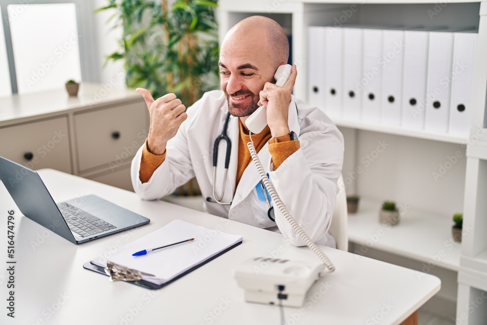 Young bald man with beard working on telephone appointment pointing thumb up to the side smiling happy with open mouth Young bald man with beard working on telephone appointment pointing thumb up to the side smiling happy with open mouth