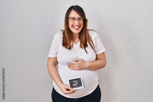 Pregnant woman holding baby ecography smiling and laughing hard out loud because funny crazy joke.