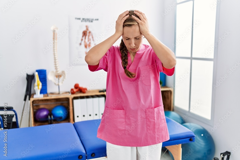 Young blonde woman working at pain recovery clinic suffering from headache desperate and stressed because pain and migraine. hands on head. Young blonde woman working at pain recovery clinic suffering from headache desperate and stressed because pain and migraine. hands on head.