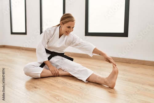 Young caucasian woman wearing karate uniform stretching at sport center