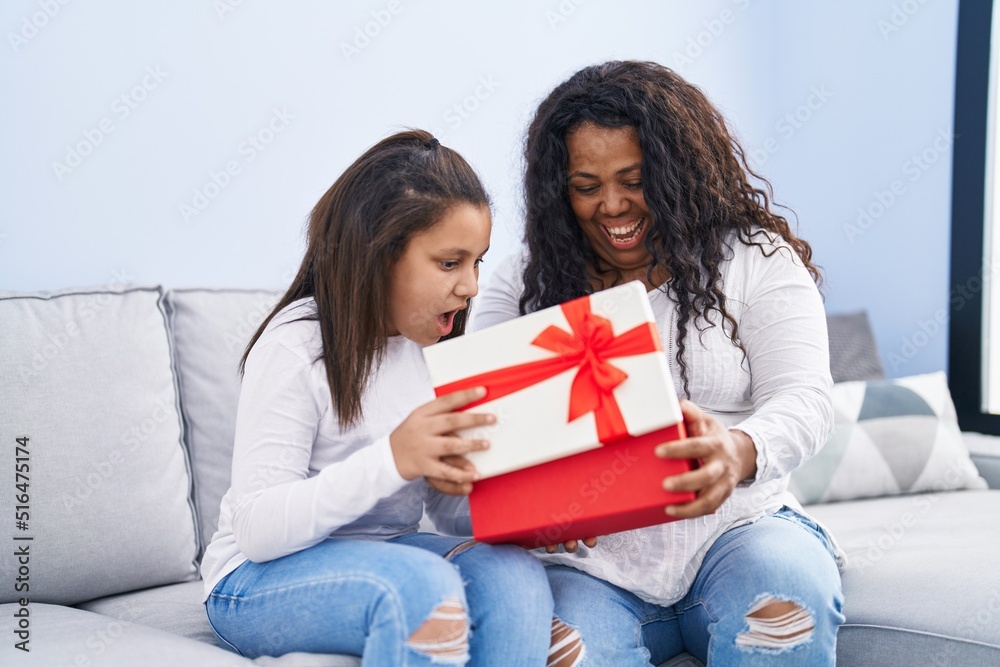 Mother and daughter unpack gift sitting on sofa at home Mother and daughter unpack gift sitting on sofa at home
