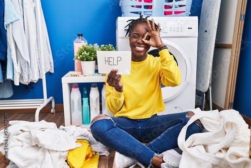 Beautiful black woman doing laundry asking for help smiling happy doing ok sign with hand on eye looking through fingers