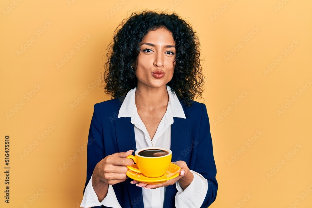 Young latin girl wearing business style drinking cup of coffee looking at the camera blowing a kiss being lovely and sexy. love expression. Young latin girl wearing business style drinking cup of coffee looking at the camera blowing a kiss being lovely and sexy. love expression.