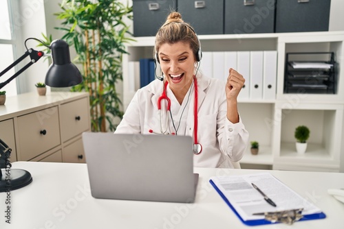 Young doctor woman wearing doctor uniform working using computer laptop screaming proud, celebrating victory and success very excited with raised arms photo