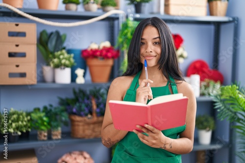 Young hispanic woman florist reading book at florist shop