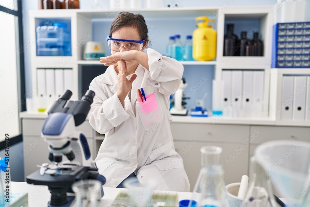 Hispanic girl with down syndrome working at scientist laboratory doing time out gesture with hands, frustrated and serious face