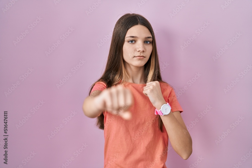 Teenager girl standing over pink background punching fist to fight, aggressive and angry attack, threat and violence Teenager girl standing over pink background punching fist to fight, aggressive and angry attack, threat and violence