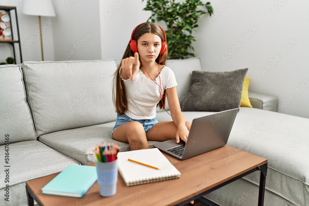 Young brunette teenager doing homework with laptop at home pointing with finger to the camera and to you, confident gesture looking serious Young brunette teenager doing homework with laptop at home pointing with finger to the camera and to you, confident gesture looking serious