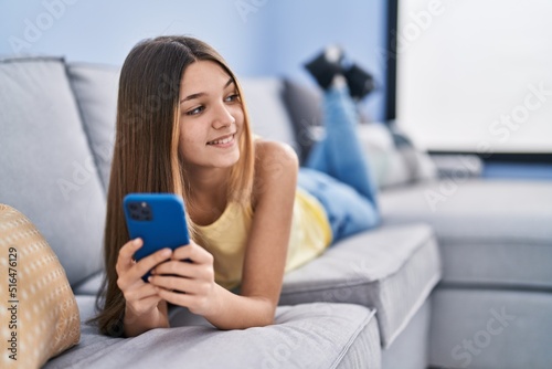 Adorable girl using smartphone lying on sofa at home