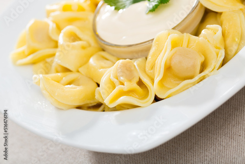 Closeup of traditional Italian ravioli served on white plate with sour cream sauce photo