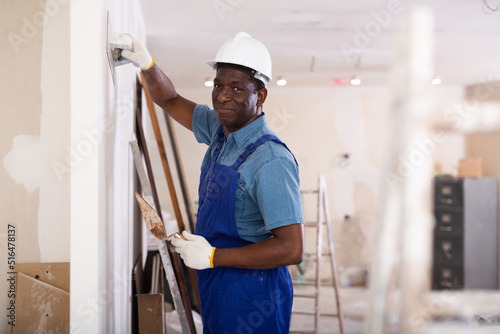 African american contractor doing repairs in a new building plasters the wall indoors