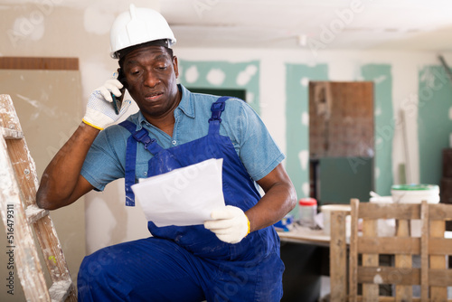 Worker in blue overalls communicates on a mobile phone in a renovated room