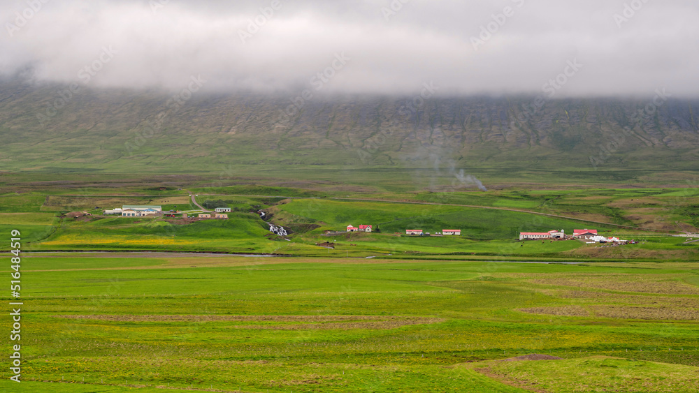 Fields and farmhouse in front of mountains under cloudy day in Iceland