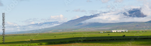 Fields and farmhouse in front of mountains under cloudy day in Iceland