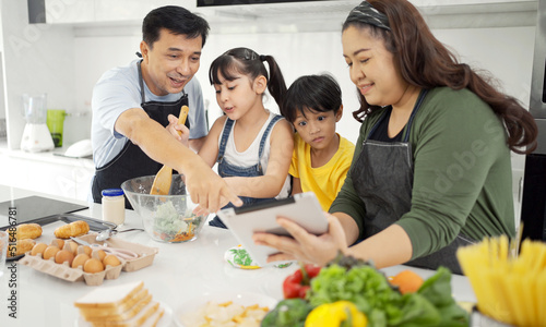 Happy asian parents and their kids having fun while cooking and following recipe on the internet.