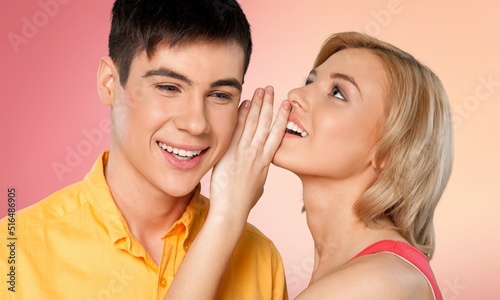 Smiling lady sharing secret or whispering gossips into her boyfriend's ear, sharing shocking news, discussing rumors