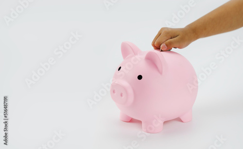Hand little girl putting coin to piggy bank isolated on white background.
