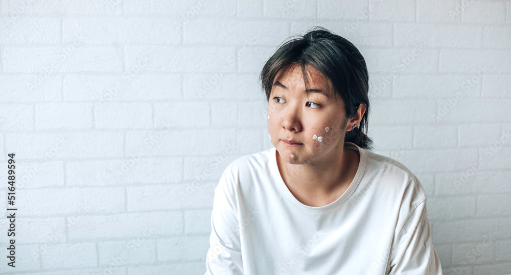 teenage girl with problematic skin, with a therapeutic cream applied. white brick wall background teenage girl with problematic skin, with a therapeutic cream applied. white brick wall background