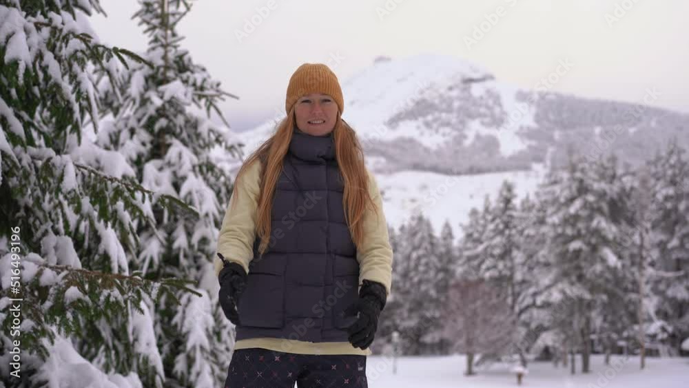Winter scene. A woman wearing an orange winter hat throws fresh snow up into the air.